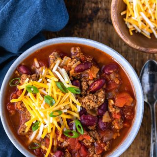 Bowl of instant pot chili topped with sliced green onions and shredded cheese