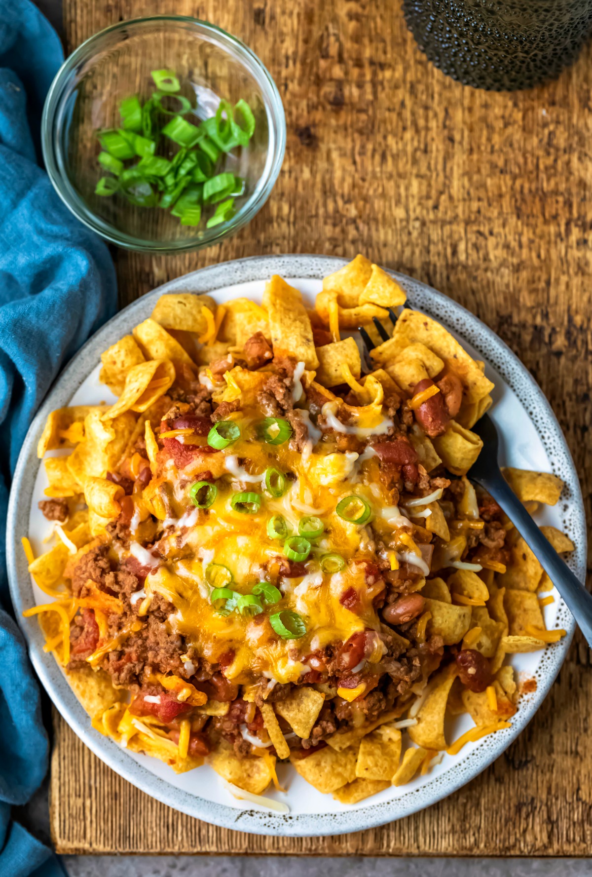 Overhead photo of a plate of chili frito pie on a wooden cutting board.