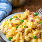 Plate of macaroni and cheese with ham and peas next to a blue linen napkin