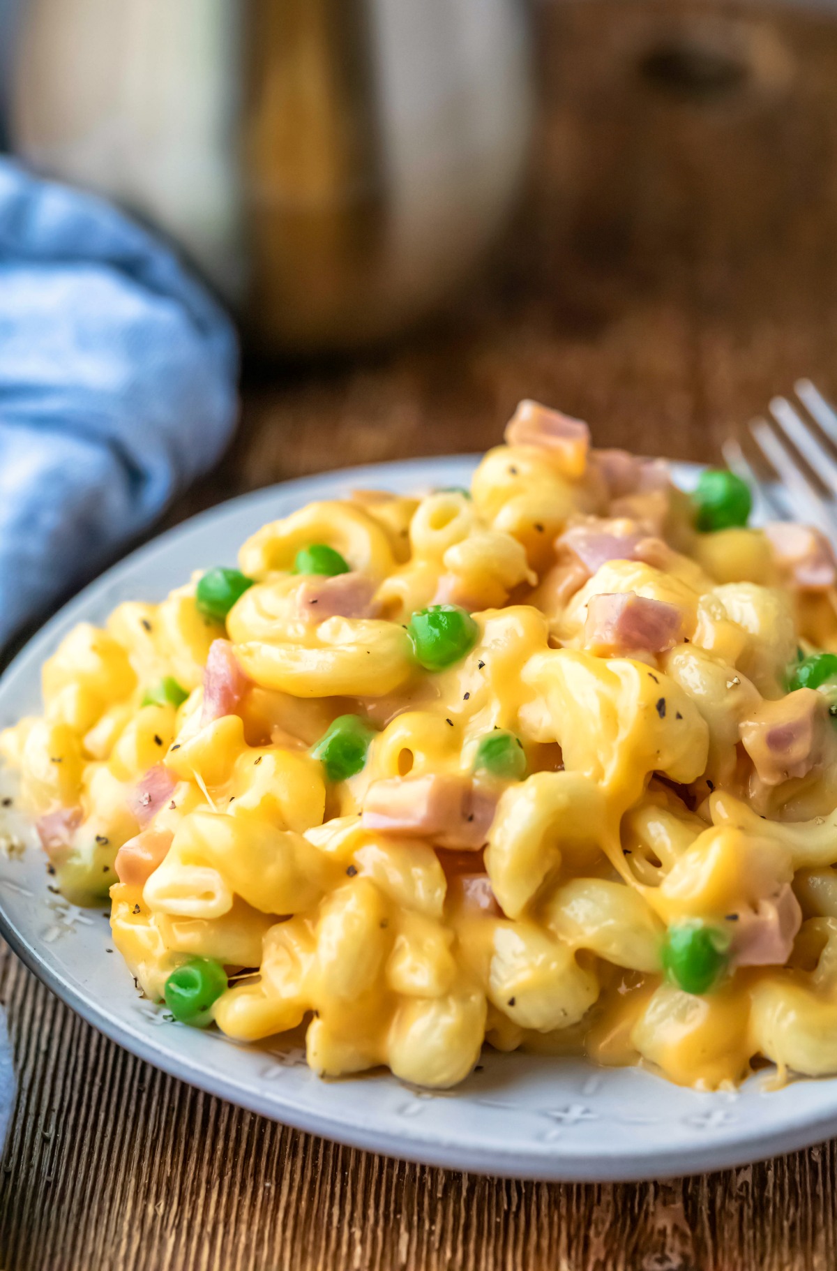 Plate of macaroni and cheese with ham and peas next to a blue linen napkin