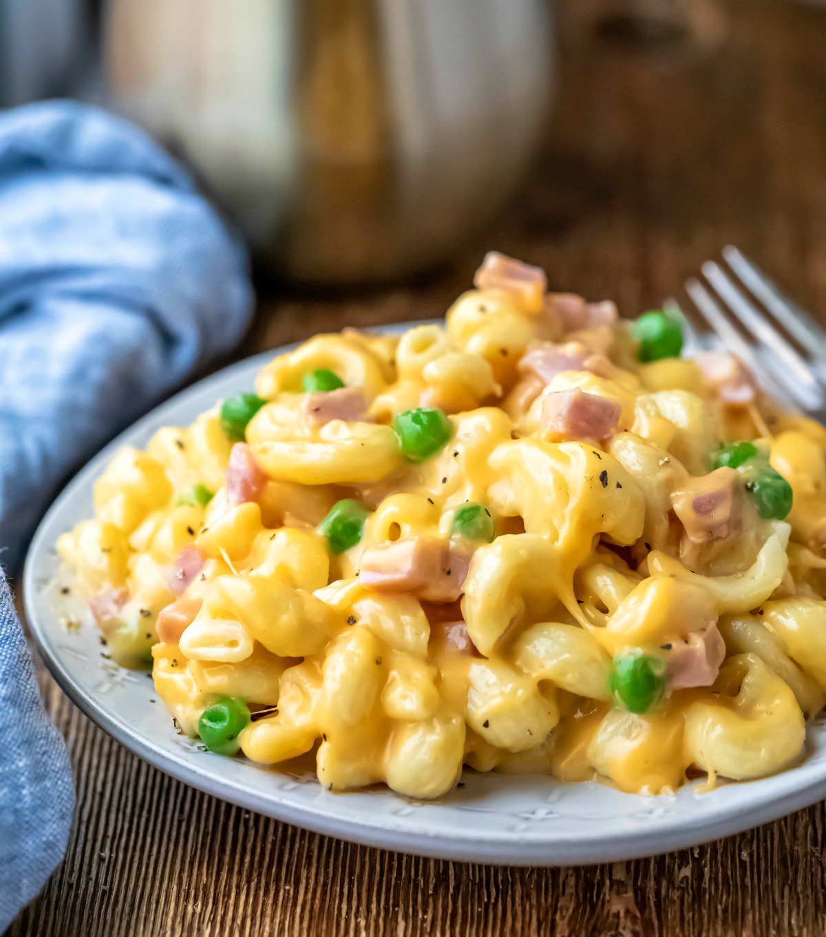 Plate of macaroni and cheese with ham and peas on a wooden cutting board