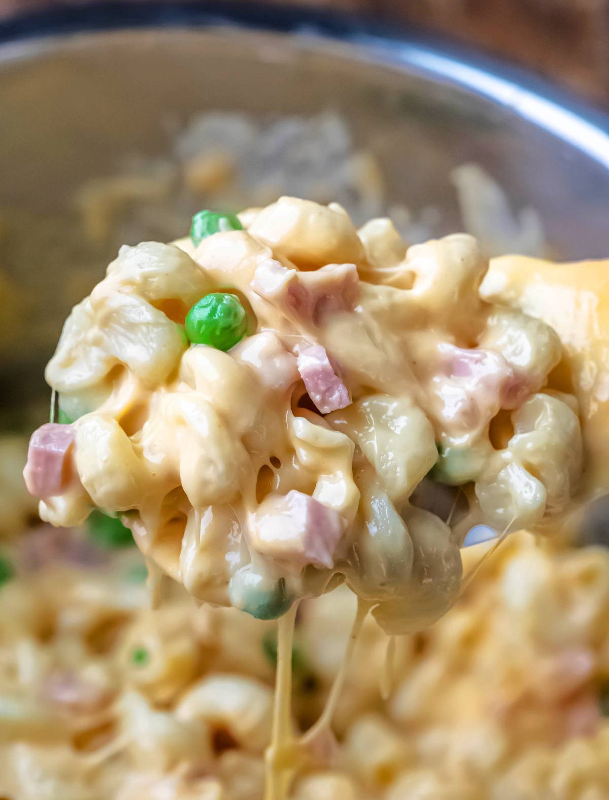 Spoon scooping up mac and cheese with ham and peas