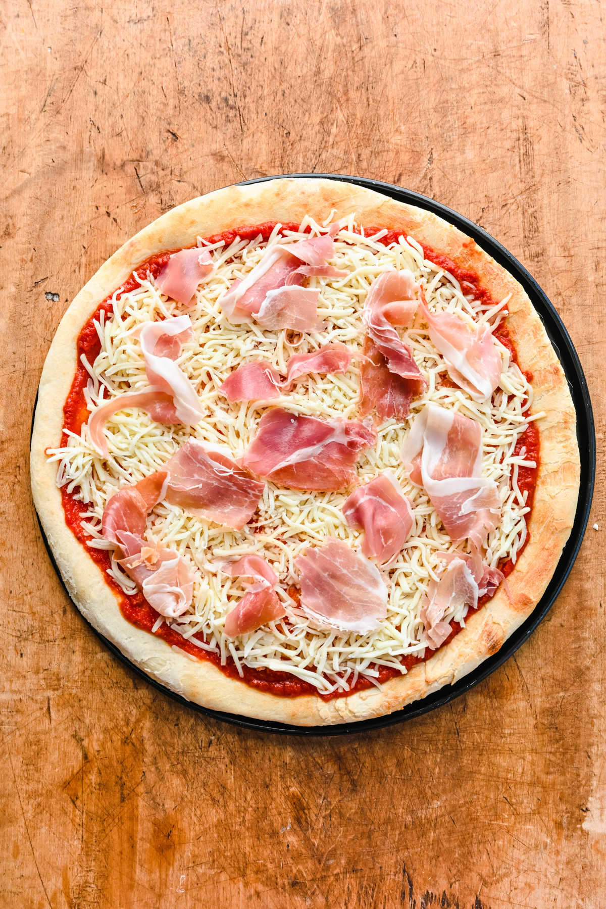 Par baked pizza crust topped with pizza sauce mozzarella and prosciutto.