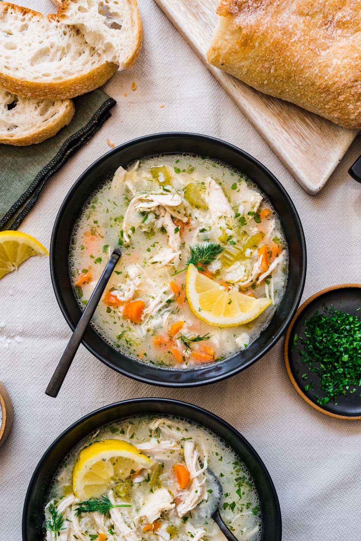 Bowls of lemon chicken and rice soup surrounded by fresh parsley and sliced bread. 