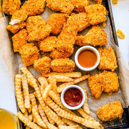 A tray of crunchy baked chicken nuggets and fries with dishes of ketchup and bbq.