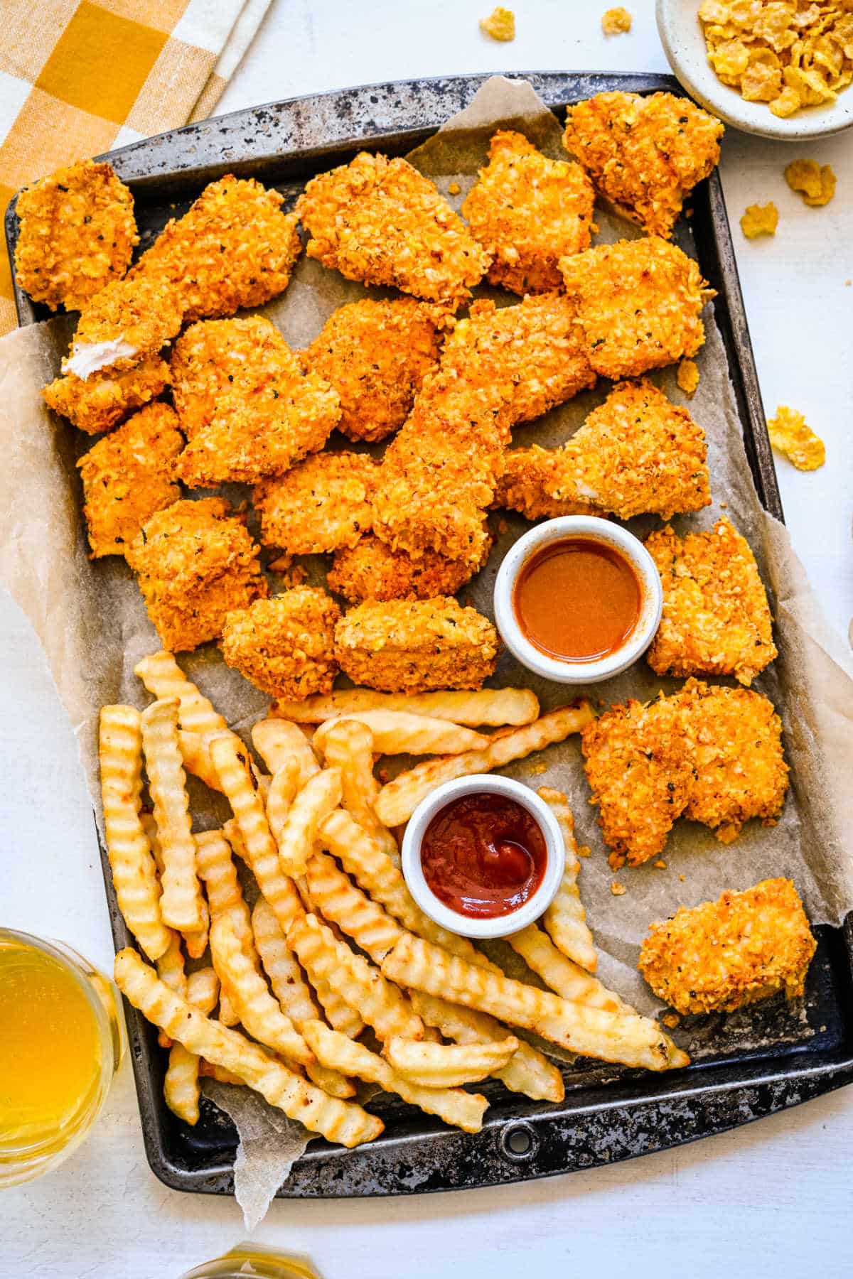 A tray of crunchy baked chicken nuggets and fries with dishes of ketchup and bbq.