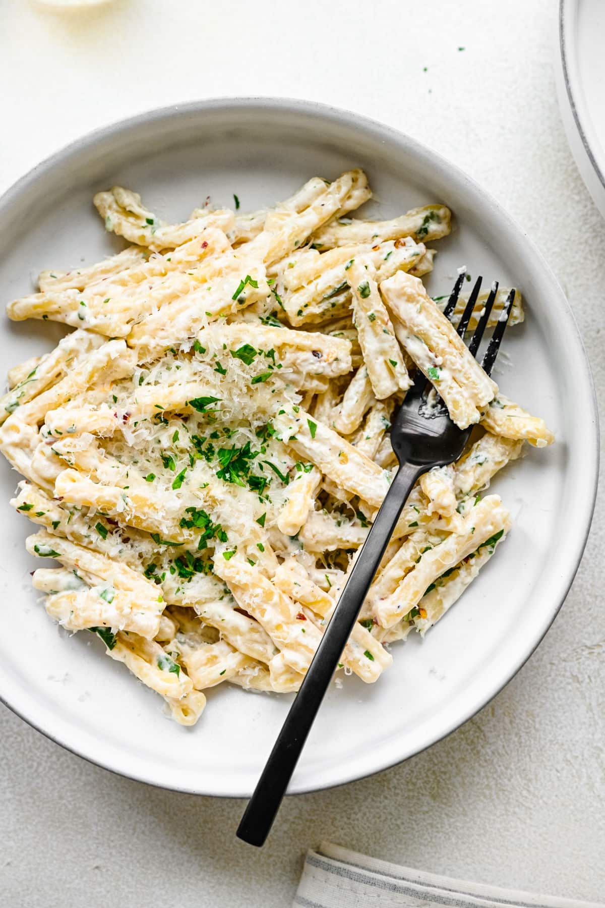 A plate of cream cheese pasta topped with shredded parsley and parmesan on it.