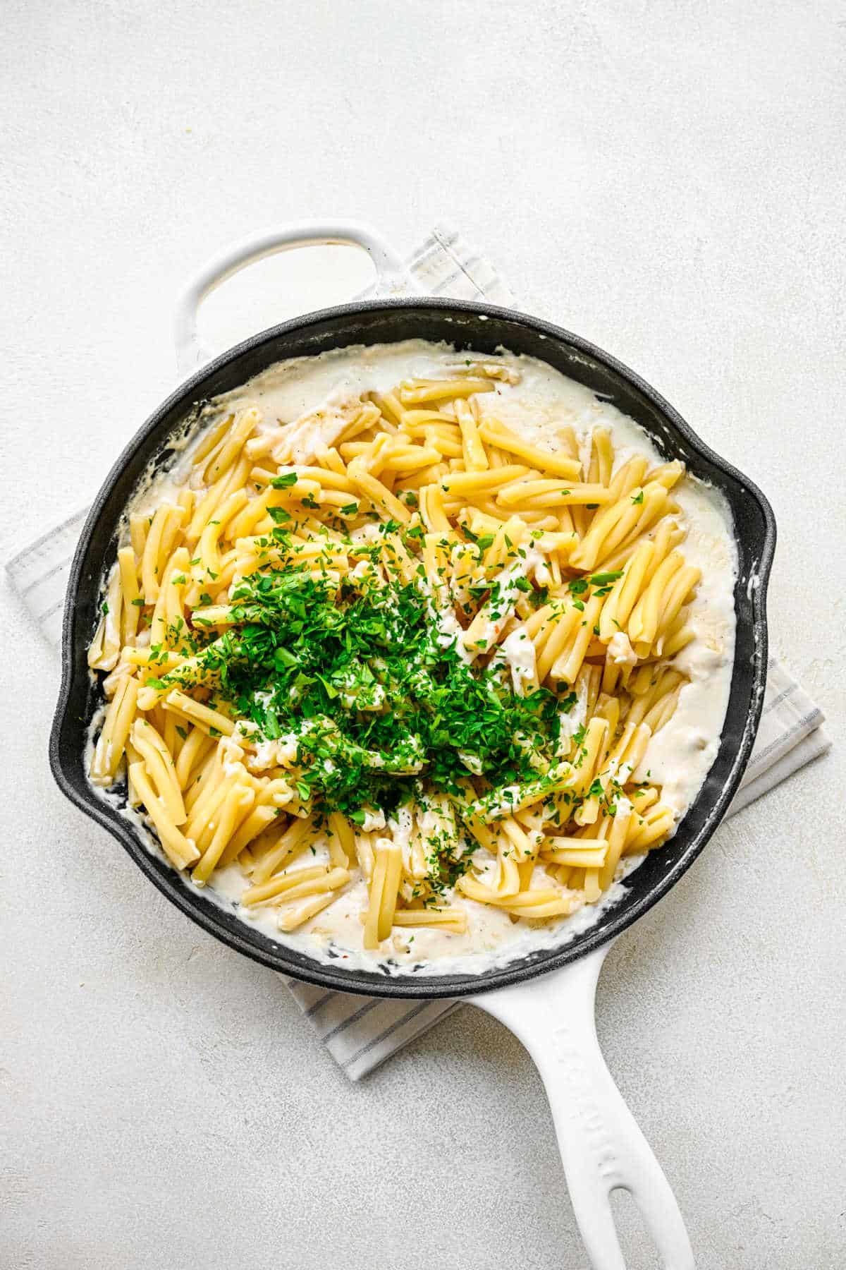 Cooked pasta and parsley on top of cream cheese mixture in a skillet. 