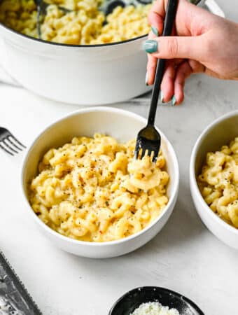 A black fork taking a bite of gouda mac and cheese in a white bowl.