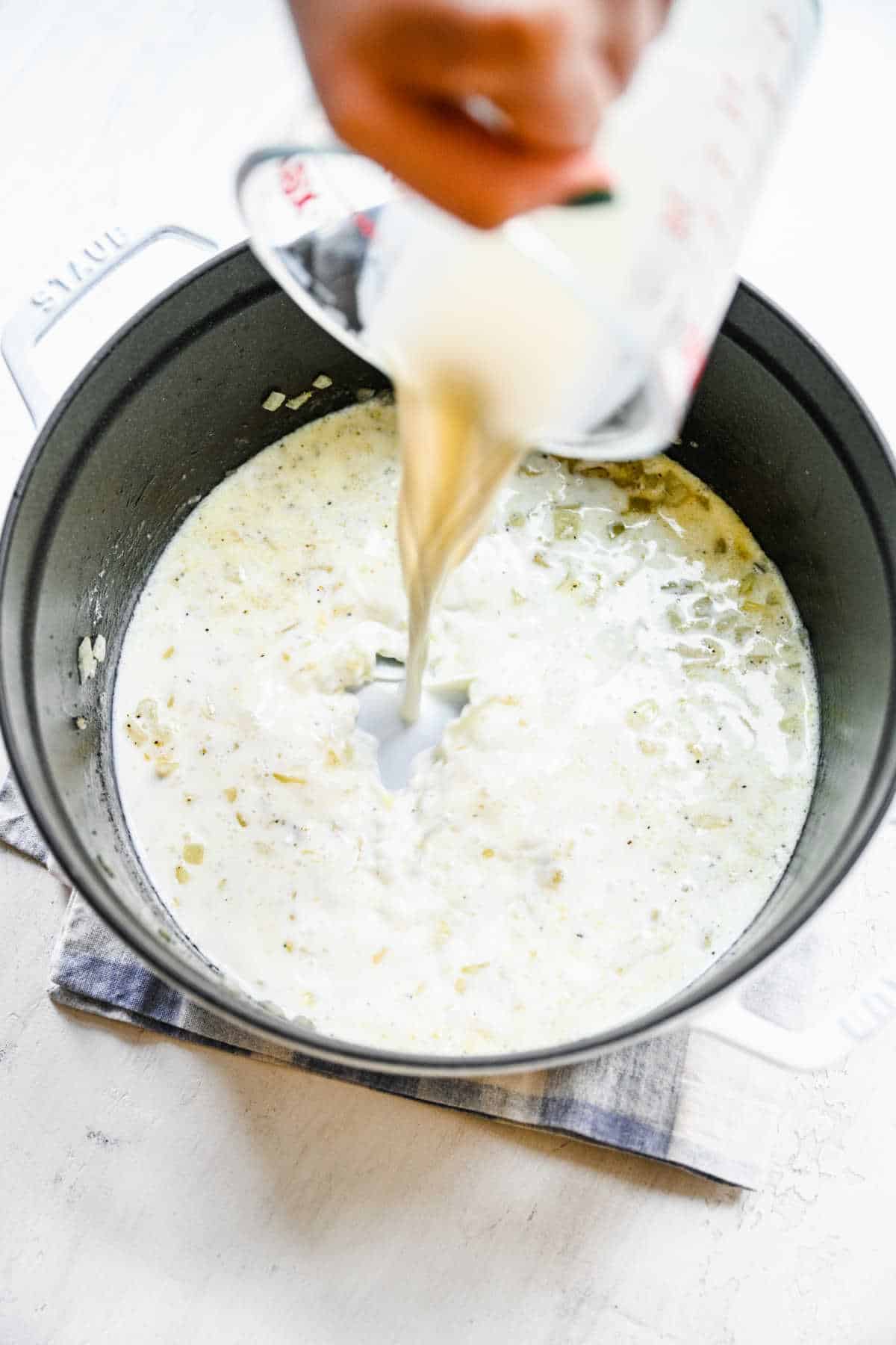 Milk pouring into onion and flour mixture in a Dutch oven.