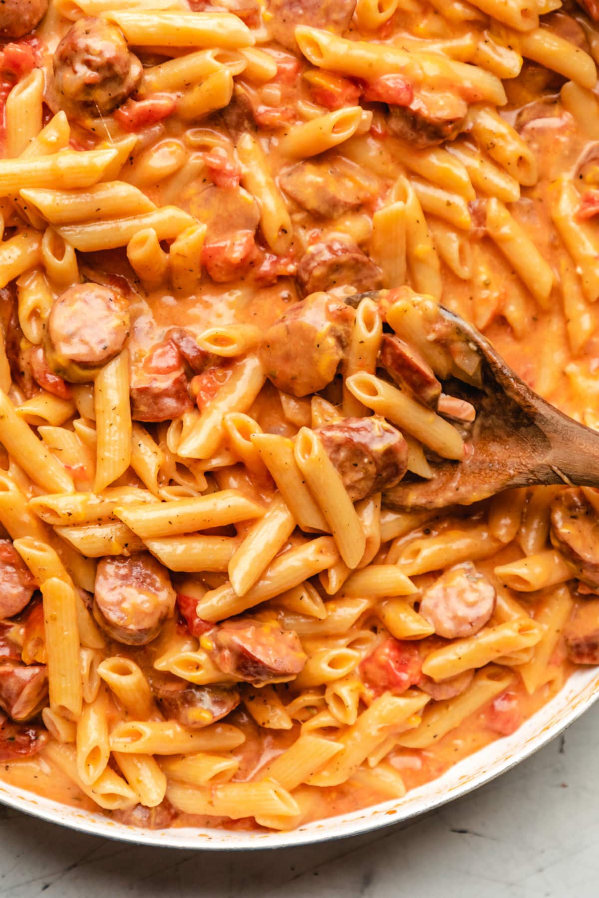 A wooden spoon scooping up cheesy kielbasa pasta. 