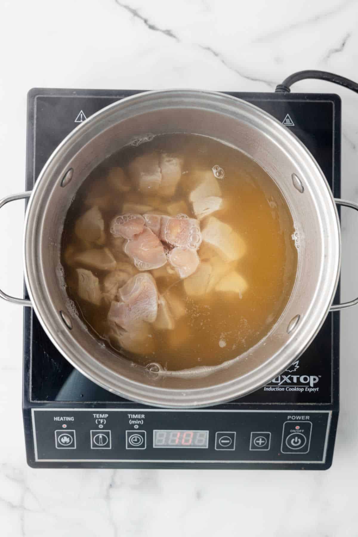 Cubed chicken breast in a pot of chicken broth.