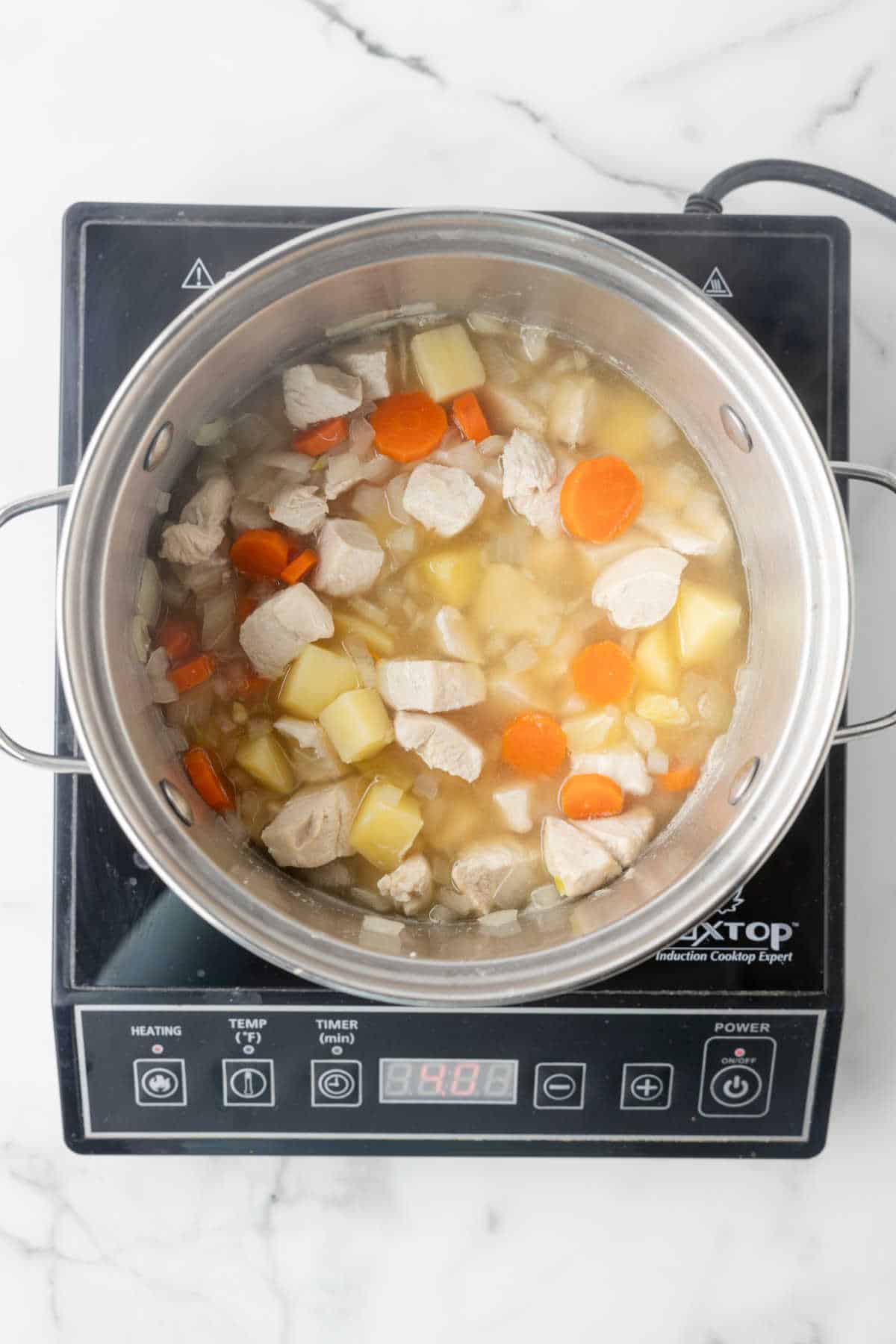 Potatoes onion and carrot cooking in a pot of chicken broth.