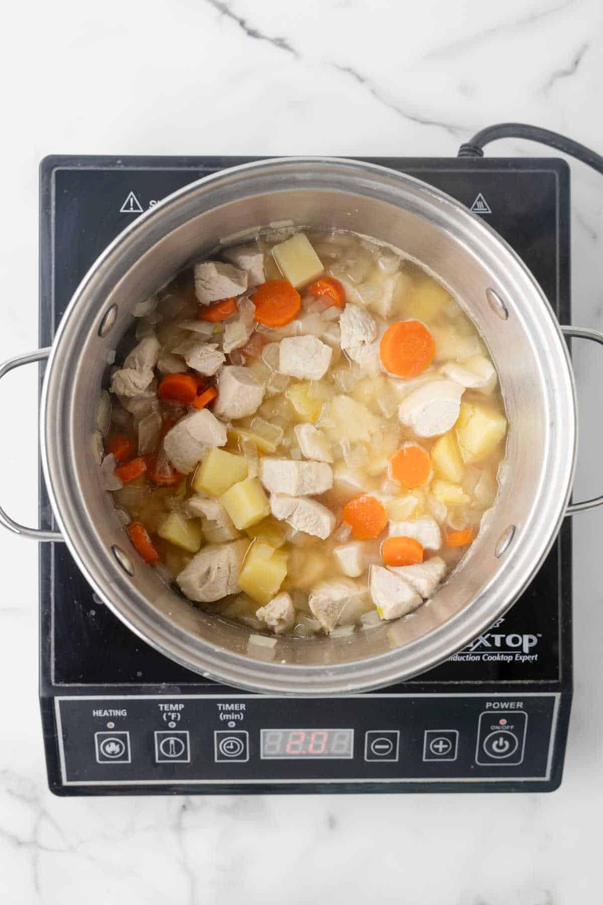 Chicken and veggies cooking in a pot of chicken broth.