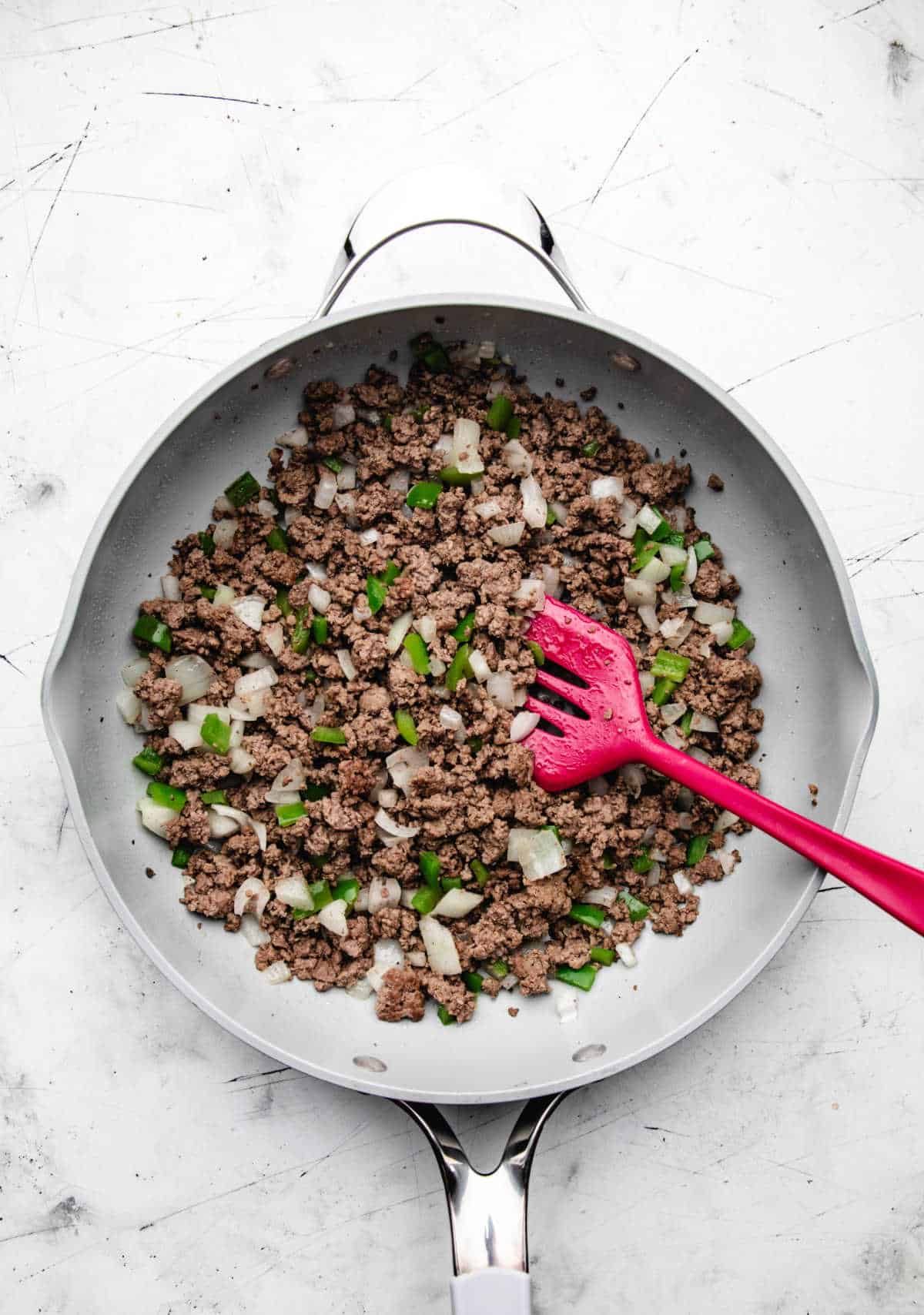 Green bell pepper and onion in ground beef in a skillet.