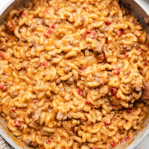 A wooden spoon in a skillet full of cheeseburger macaroni.