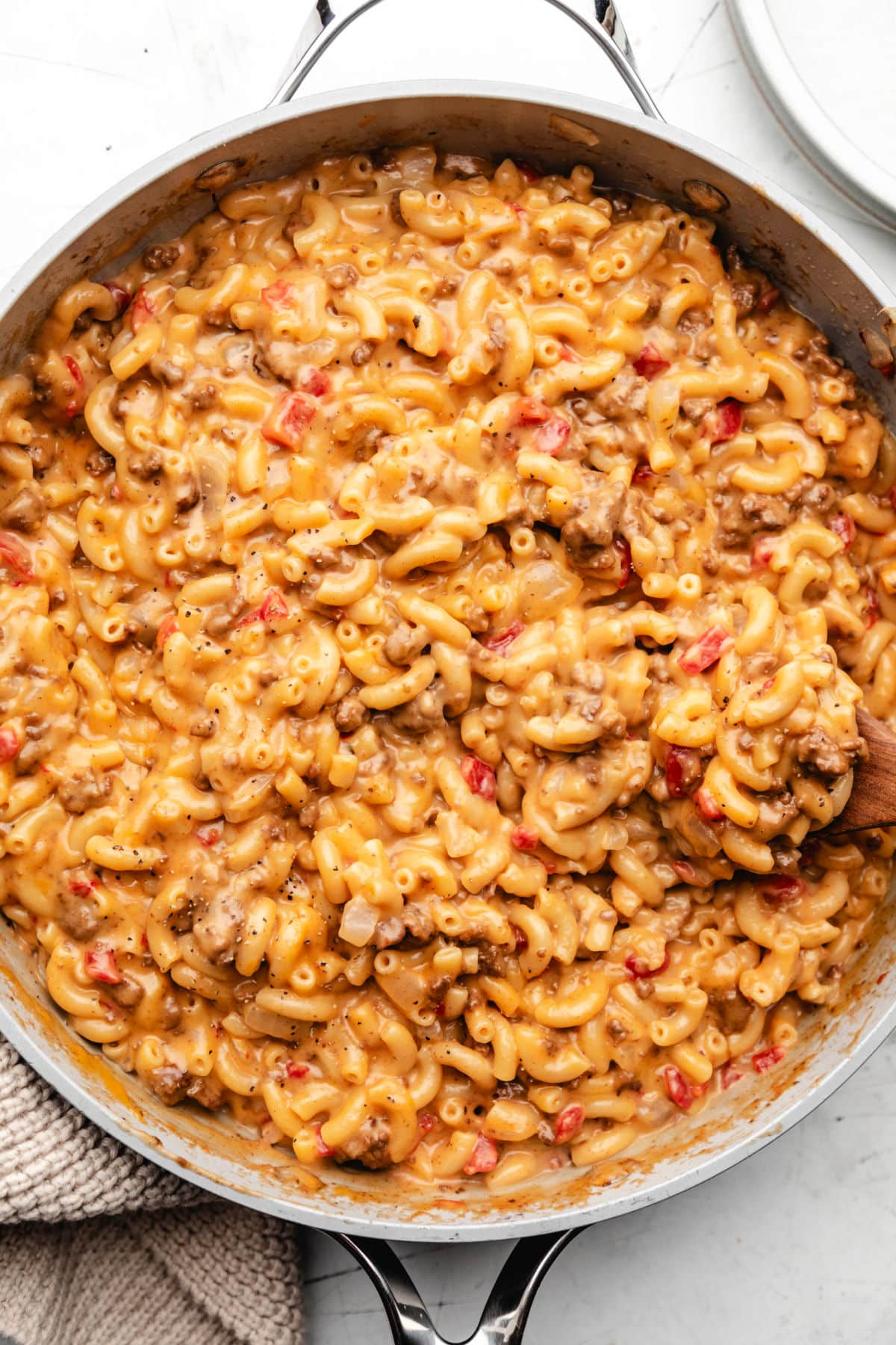 A wooden spoon in a skillet full of cheeseburger macaroni.