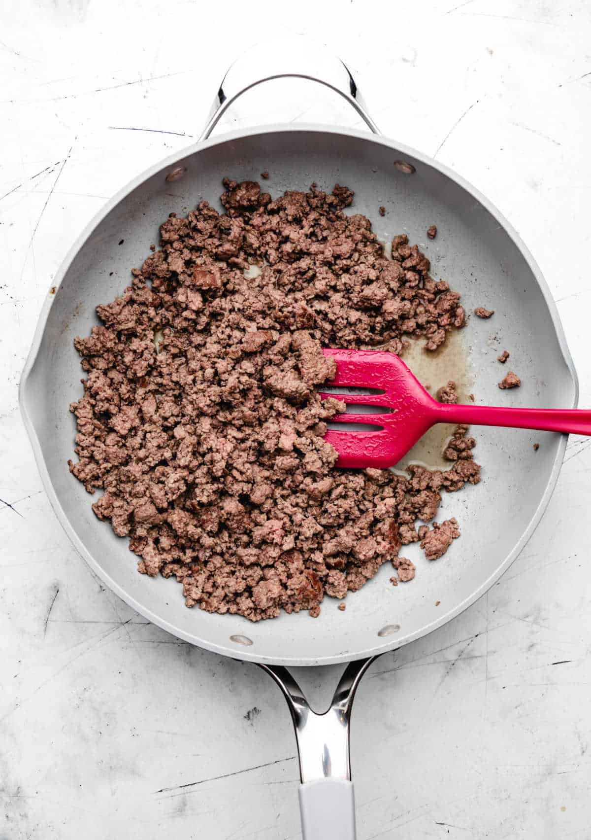 A pink spatula stirring browned ground beef in a skillet. 
