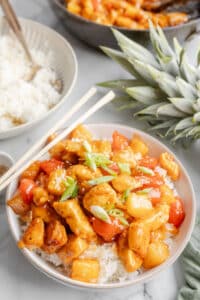 A white bowl with sweet and sour chicken on top of white rice.