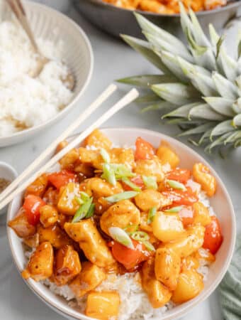 A white bowl with sweet and sour chicken on top of white rice.