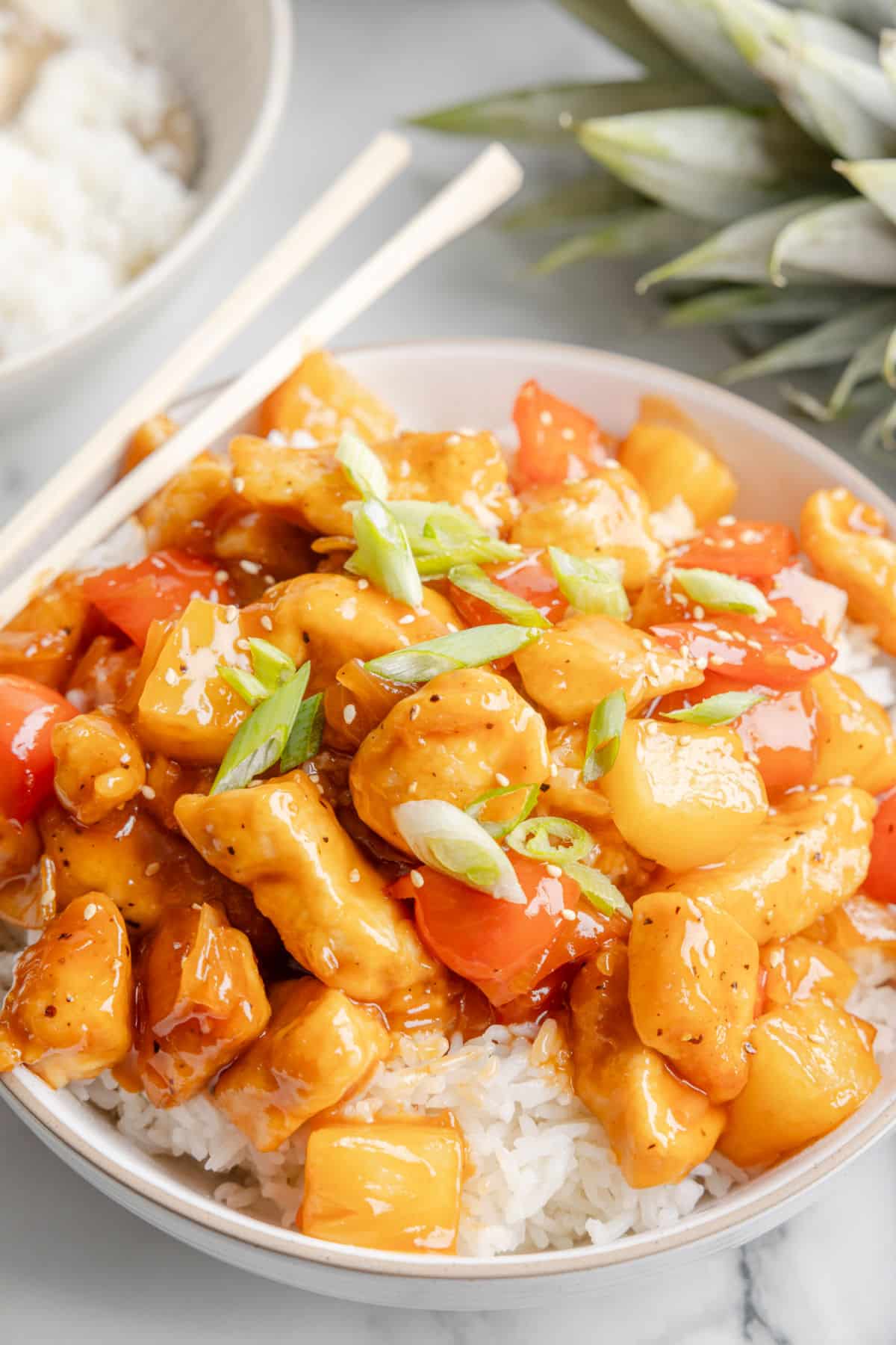 A bowl of sweet and sour chicken with two chopsticks on the side.