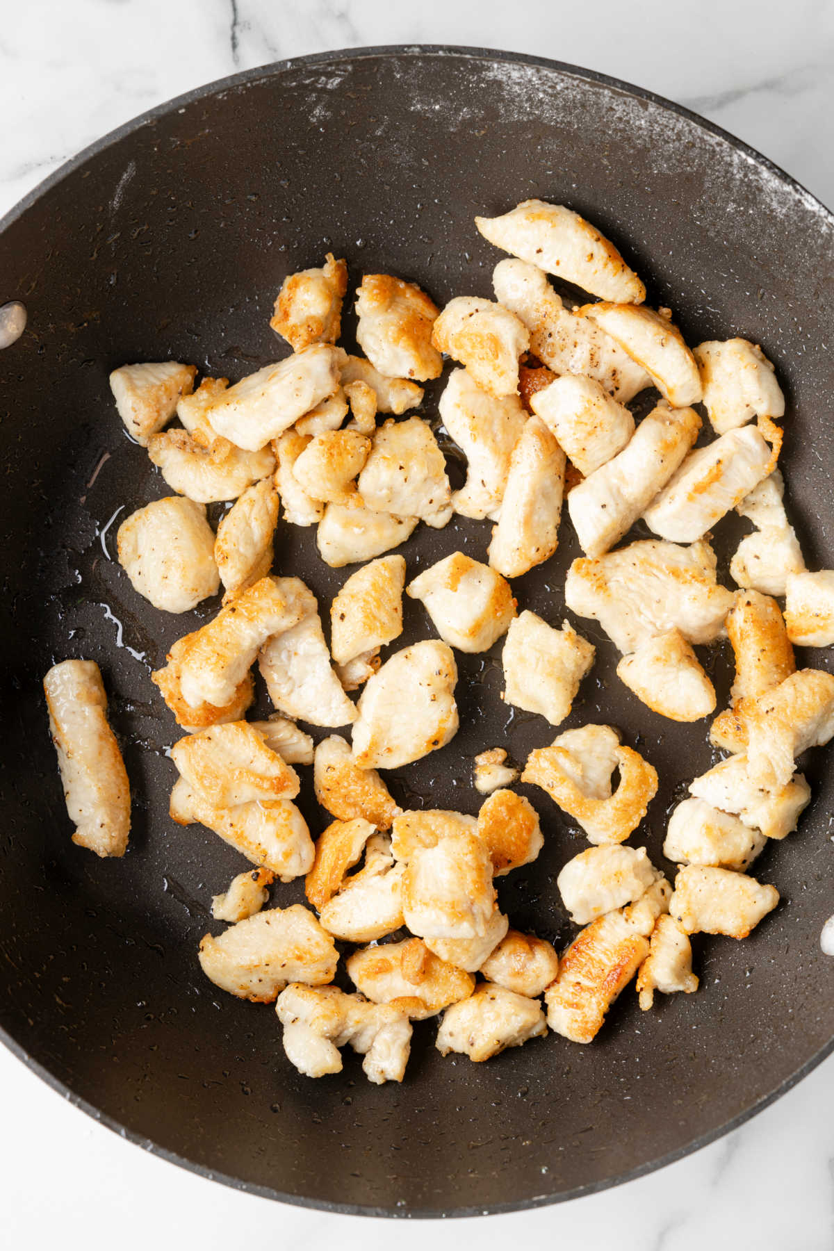 Pieces of browned chicken in a wok.