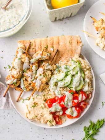 Greek chicken skewers on a bed of rice topped with tzatziki.