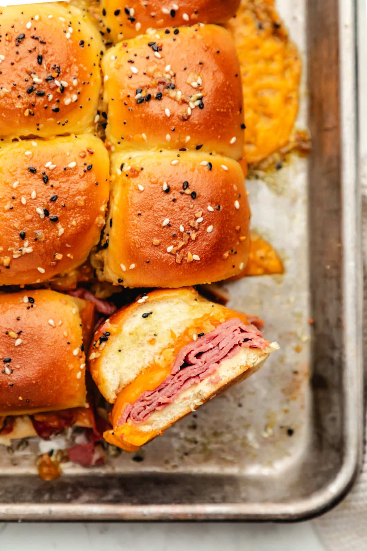 A baked roast beef slider on its side in a pan of baked sliders.