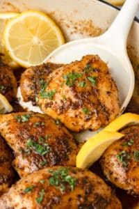 A spatula holding up a lemon herb chicken thigh from the pan.