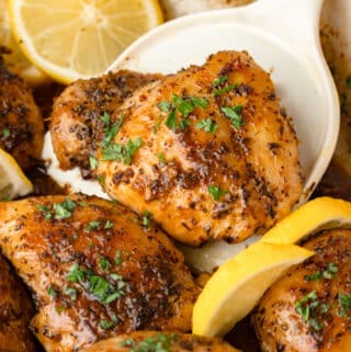 A spatula holding up a lemon herb chicken thigh from the pan.