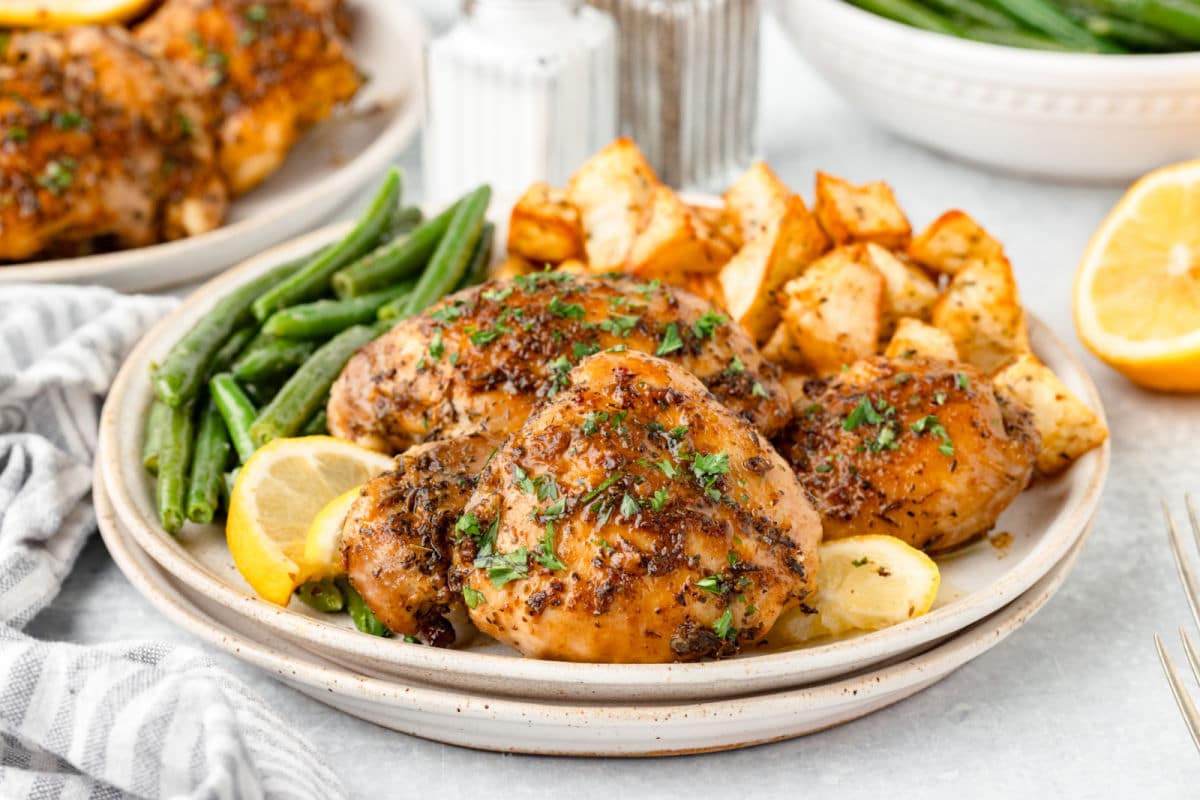 A plate of lemon herb chicken thighs potatoes and green beans with lemon wedges.
