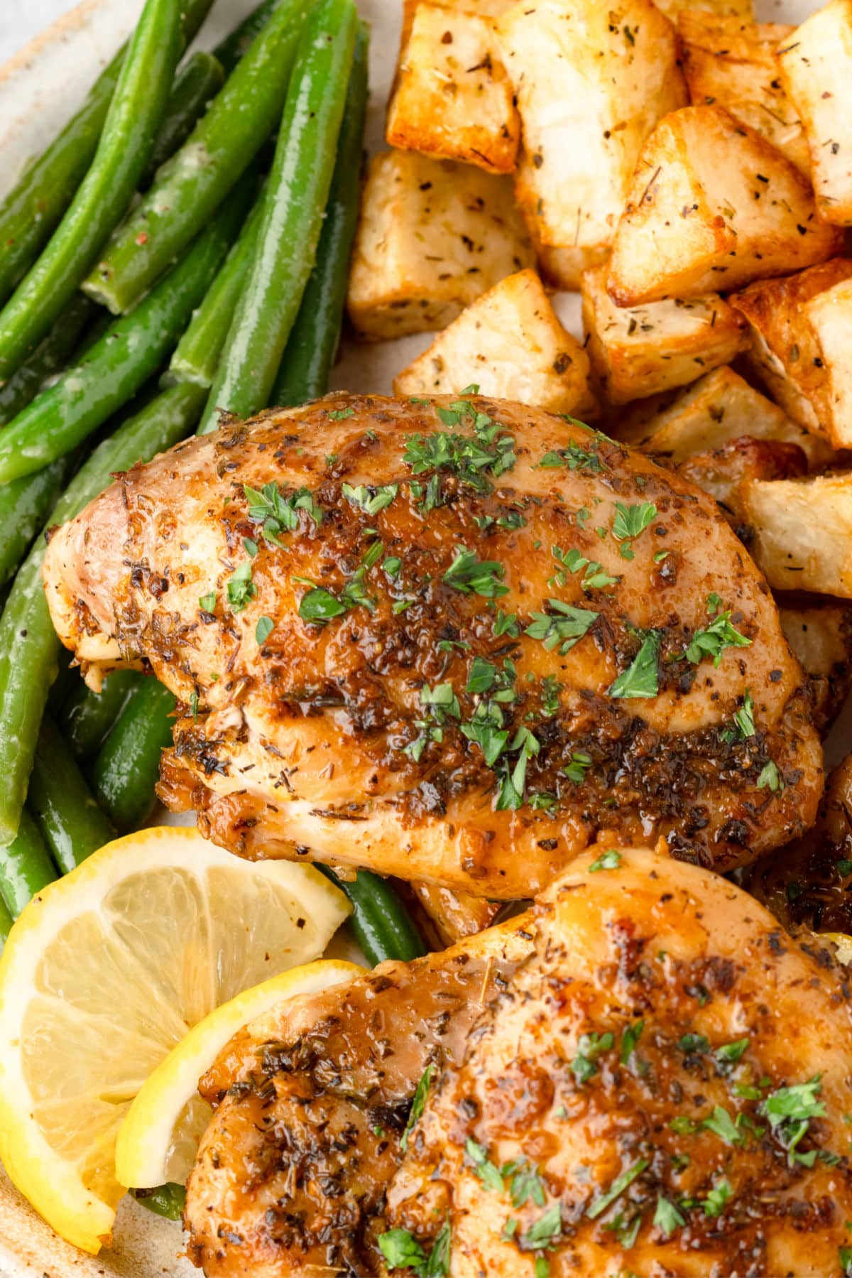Two lemon herb chicken thighs on a plate with roast potatoes and green beans.